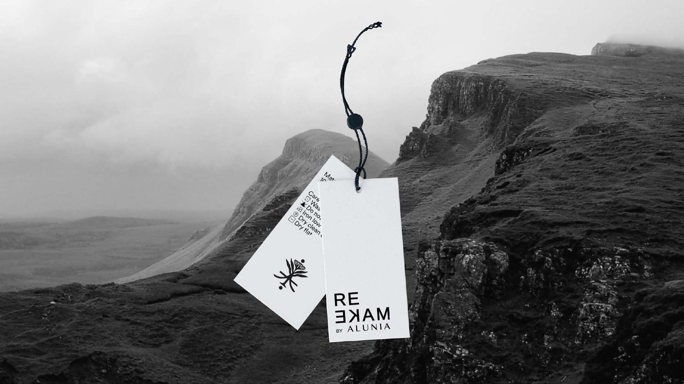 Two Remake by Alunia hang-tags on a cord against a misty mountain landscape